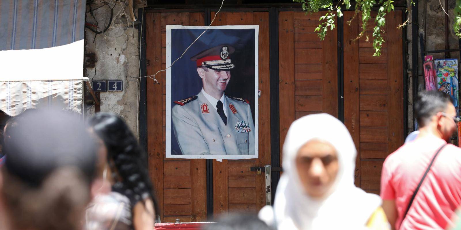 Syrian citizens walk past a door that has an Assad poster on it