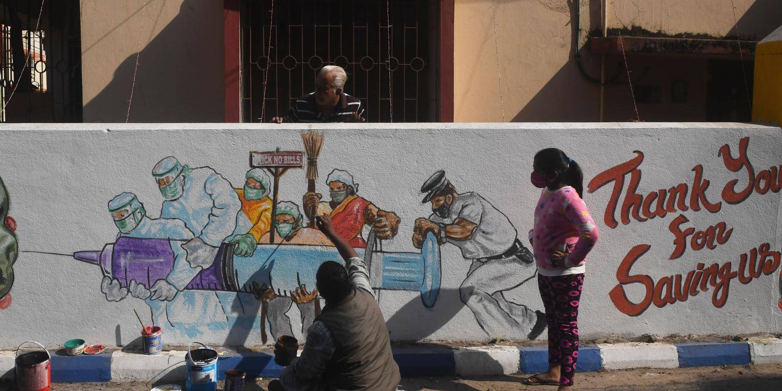 Photo shows residents with watching an artist painting a mural showing frontline workers with a COVID-19 vaccine on a street in Kolkata, India