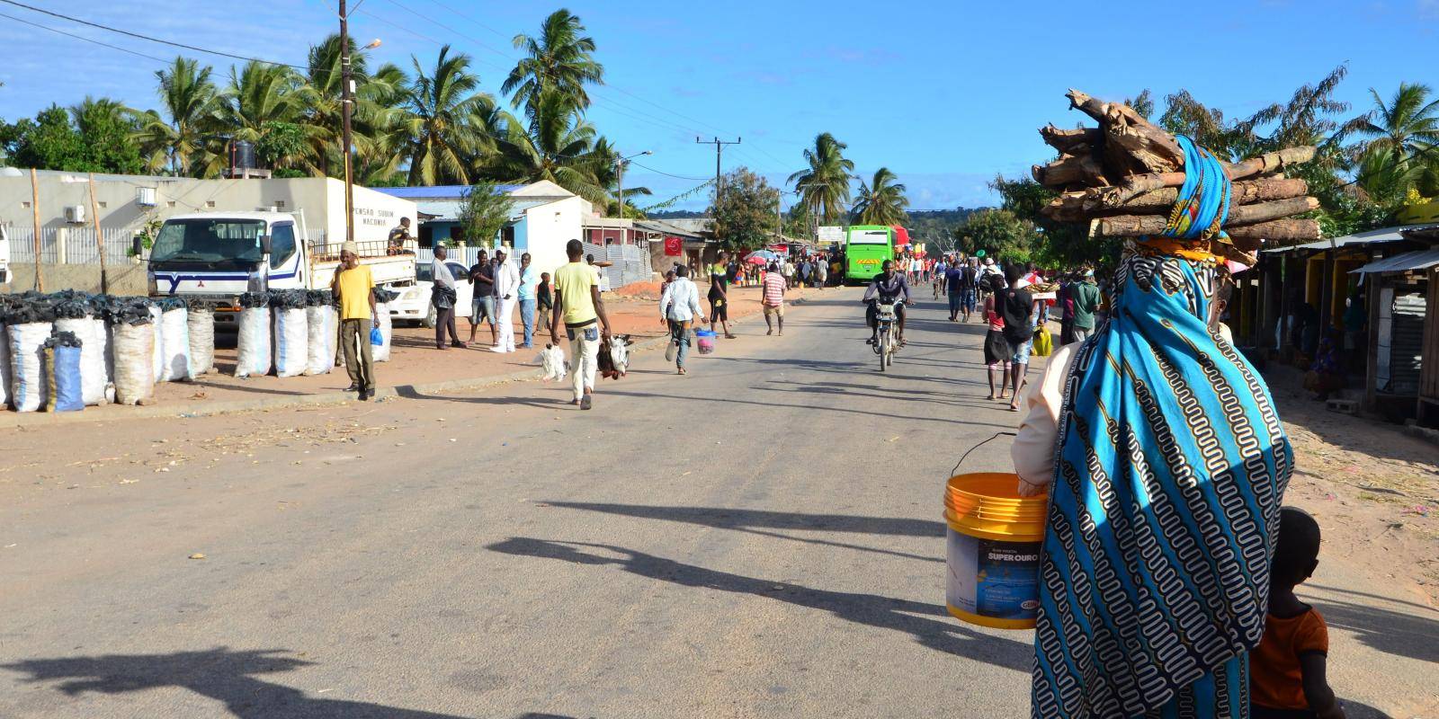 A woman carrying different items walks with her child on an unpaved suburban road