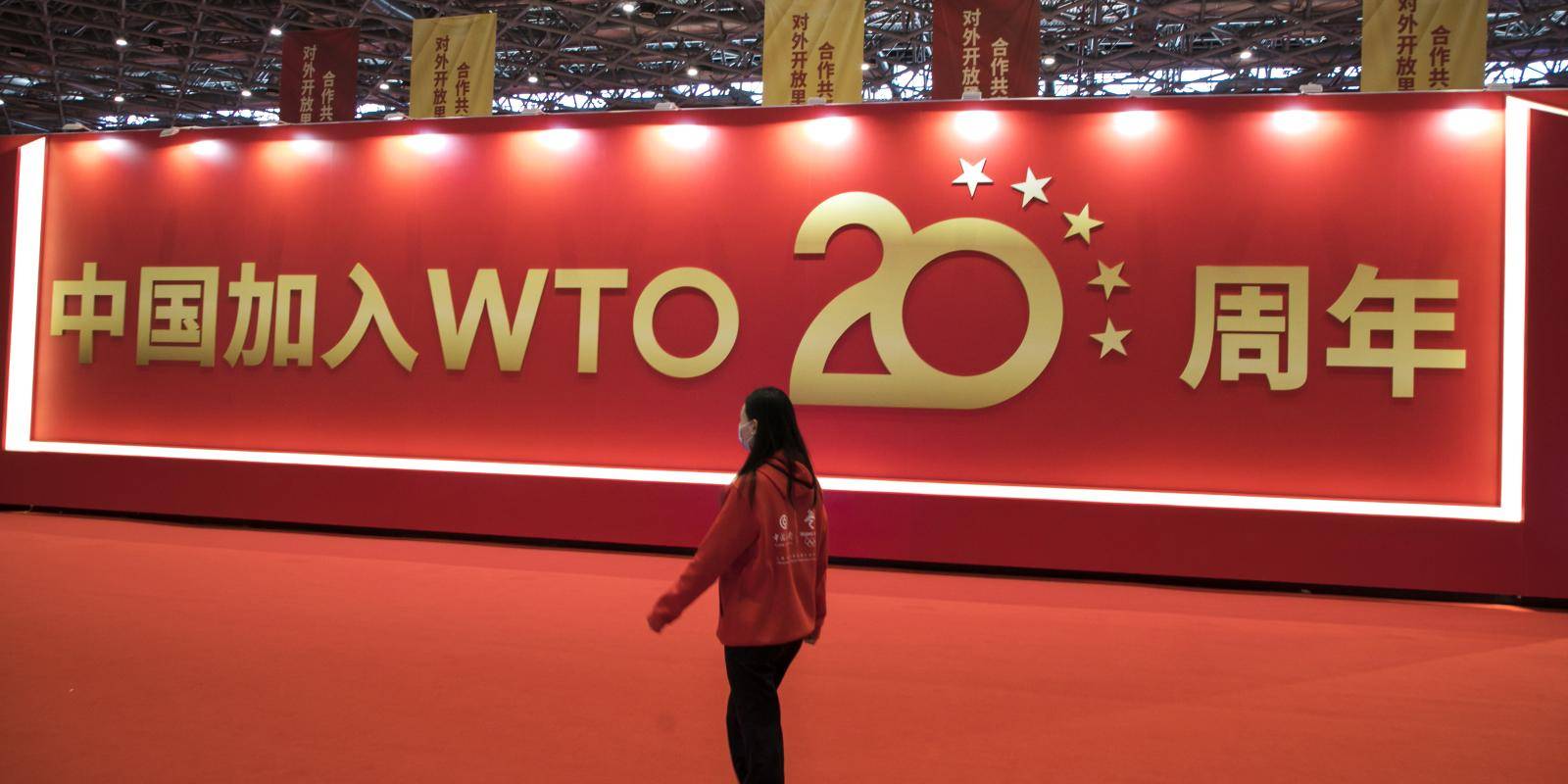 A woman walks in front of a sign celebrating the twentieth anniversary of China joining the WTO.