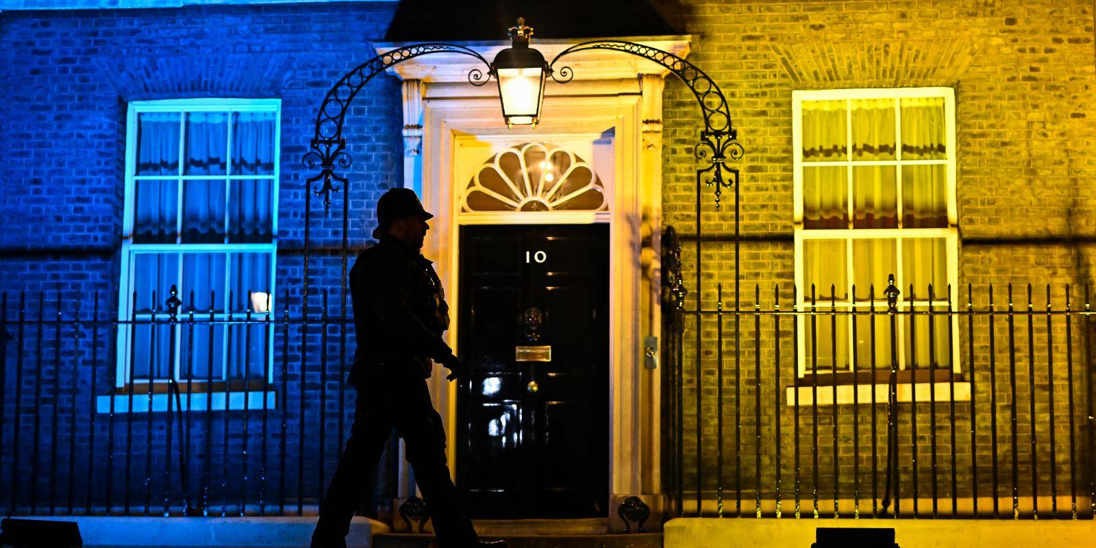 Photo shows a policeman walking in front of 10 Downing St which is lit up in the blue and yellow colours of the Ukrainian flag