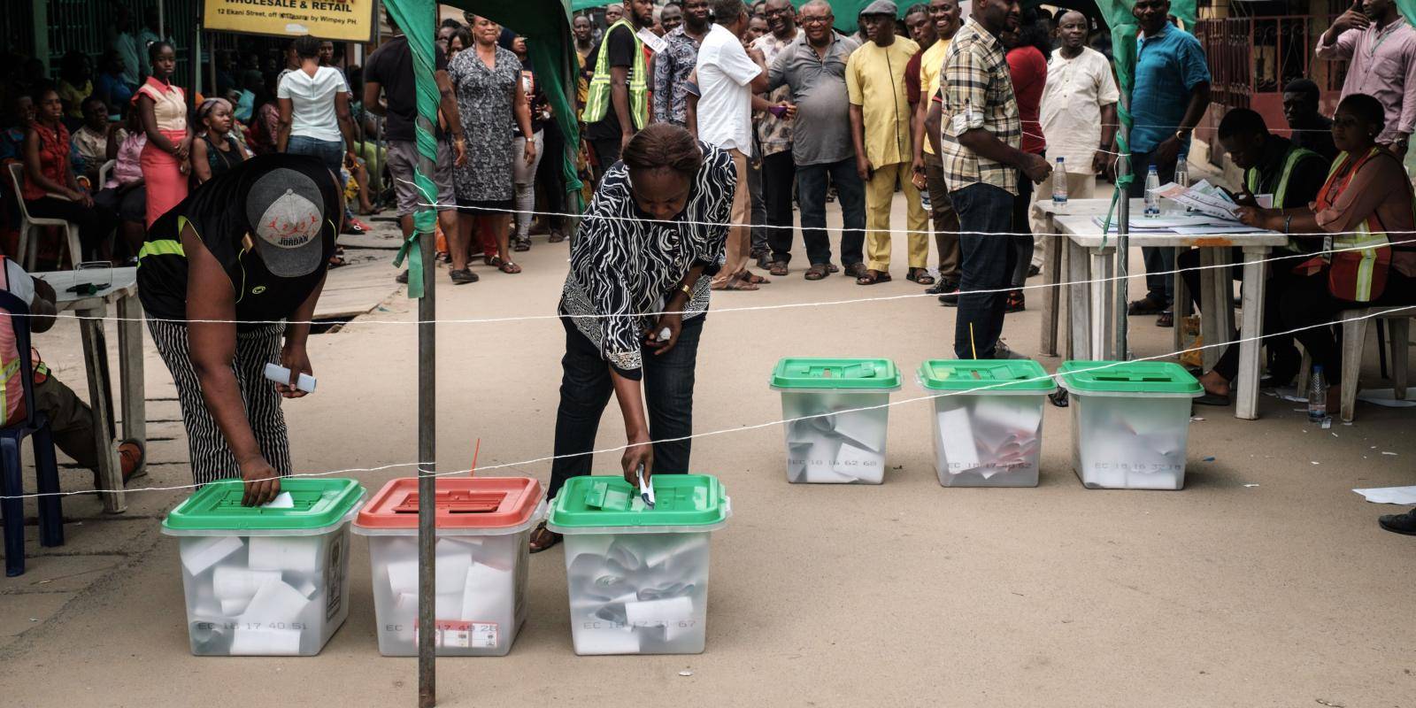 People place folded ballot papers in boxes on the ground.