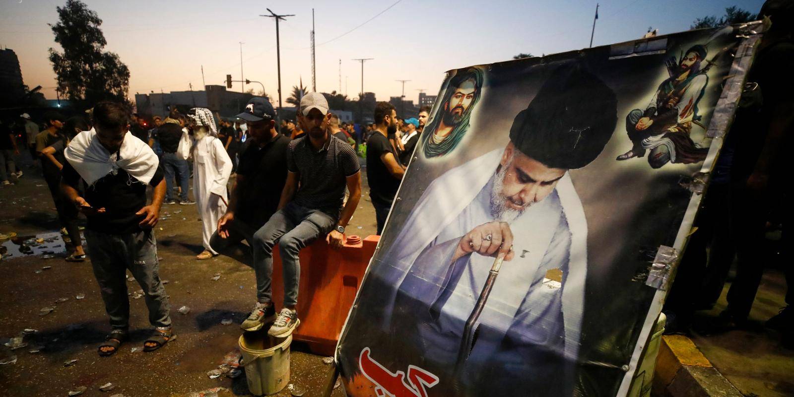 Two men wait next to a large placard of Muqtada al-Sadr