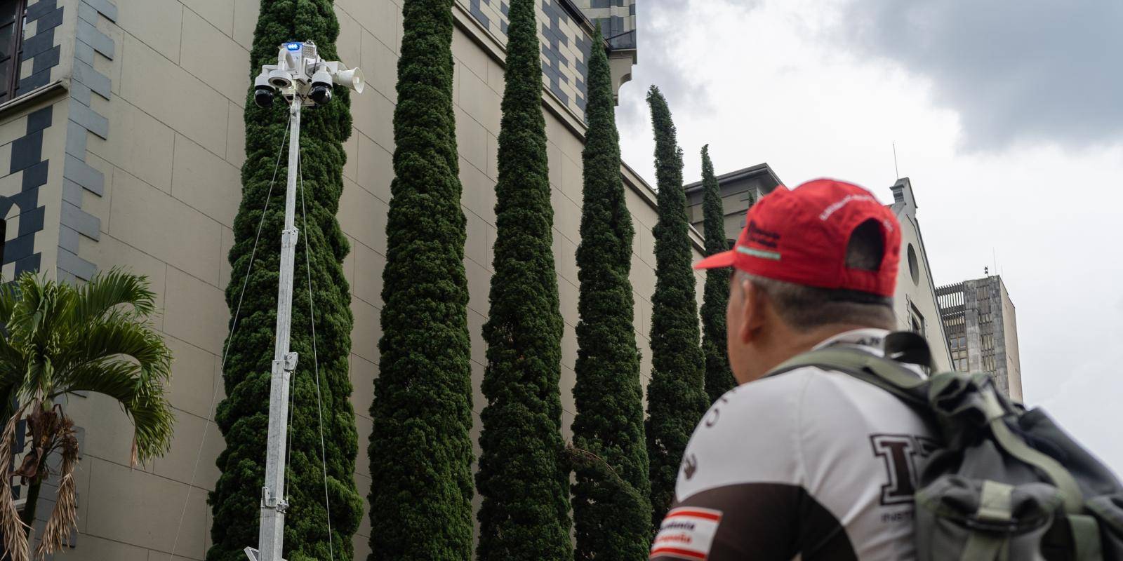 A man looks up at a solar-powered robot with three cameras and a loudspeaker attached.