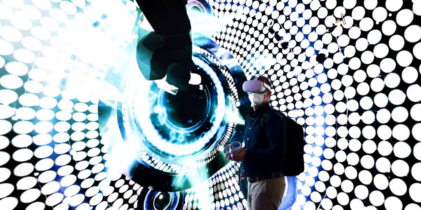A man wears a virtual reality headset in front of a brightly lit black and white dotted display screen.