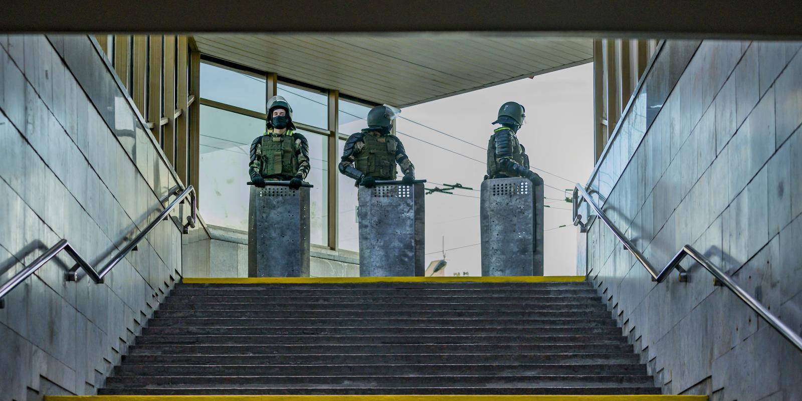 Three police officers with batons, shields and body armour stand at the top of a flight of steps