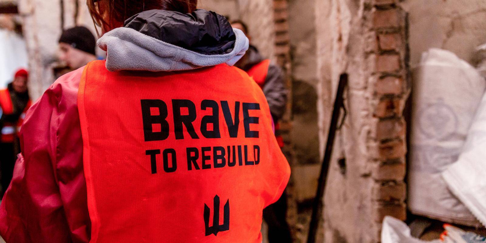 A woman wearing an orange hi-vis jacket with the logo Brave to Rebuild ...
