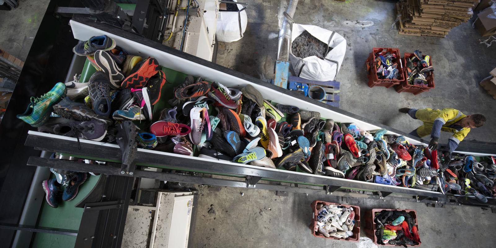 A worker places sports shoes of various colours on a conveyor belt in a shoe recycling factory.