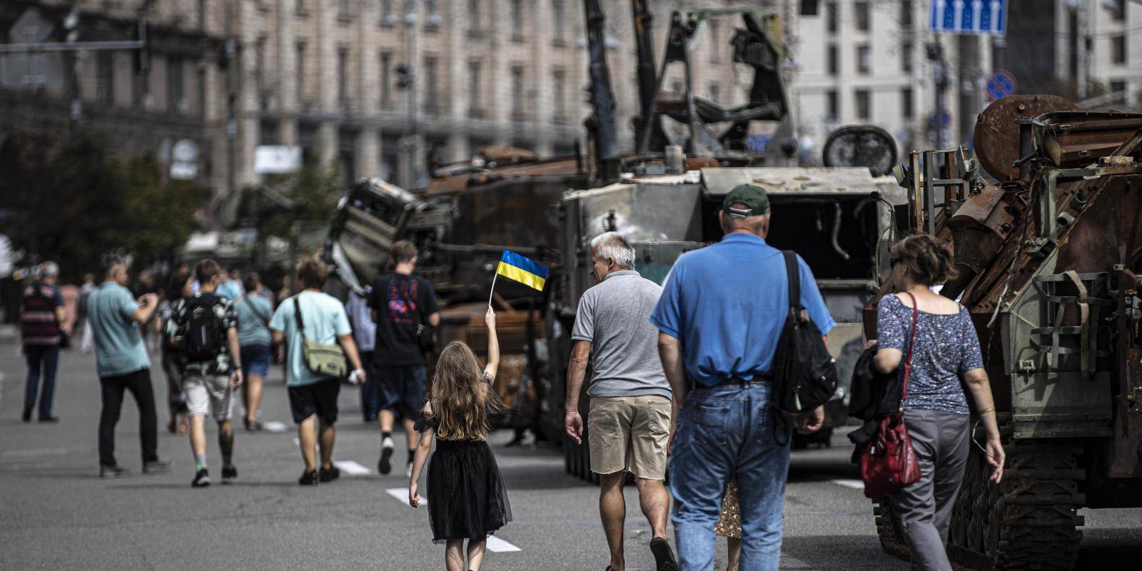 People walking down a street in Kyiv past seized military equipment including tanks and motorized artillery.