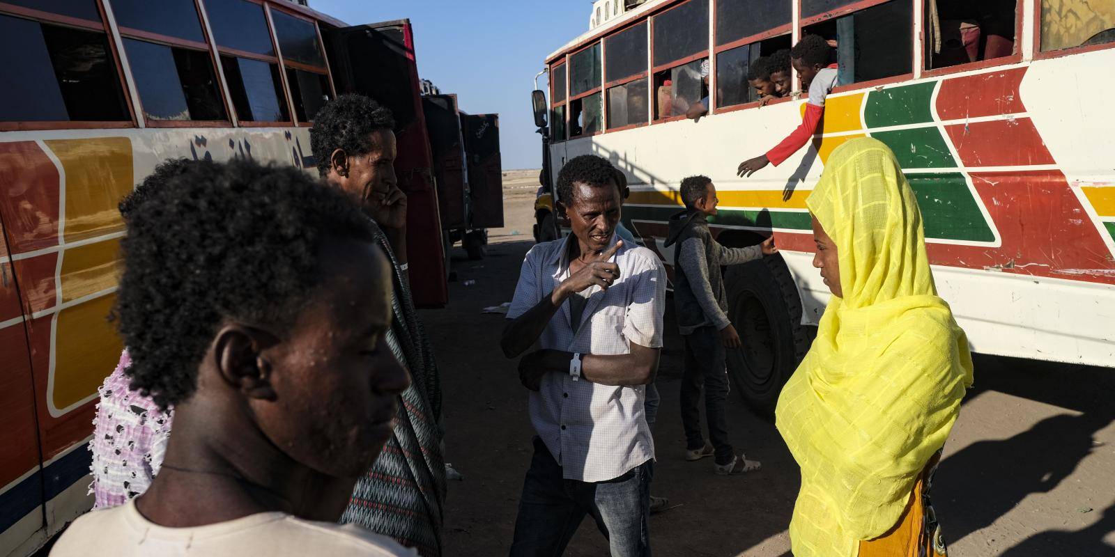 Five people are in the foreground in front of two full buses of people
