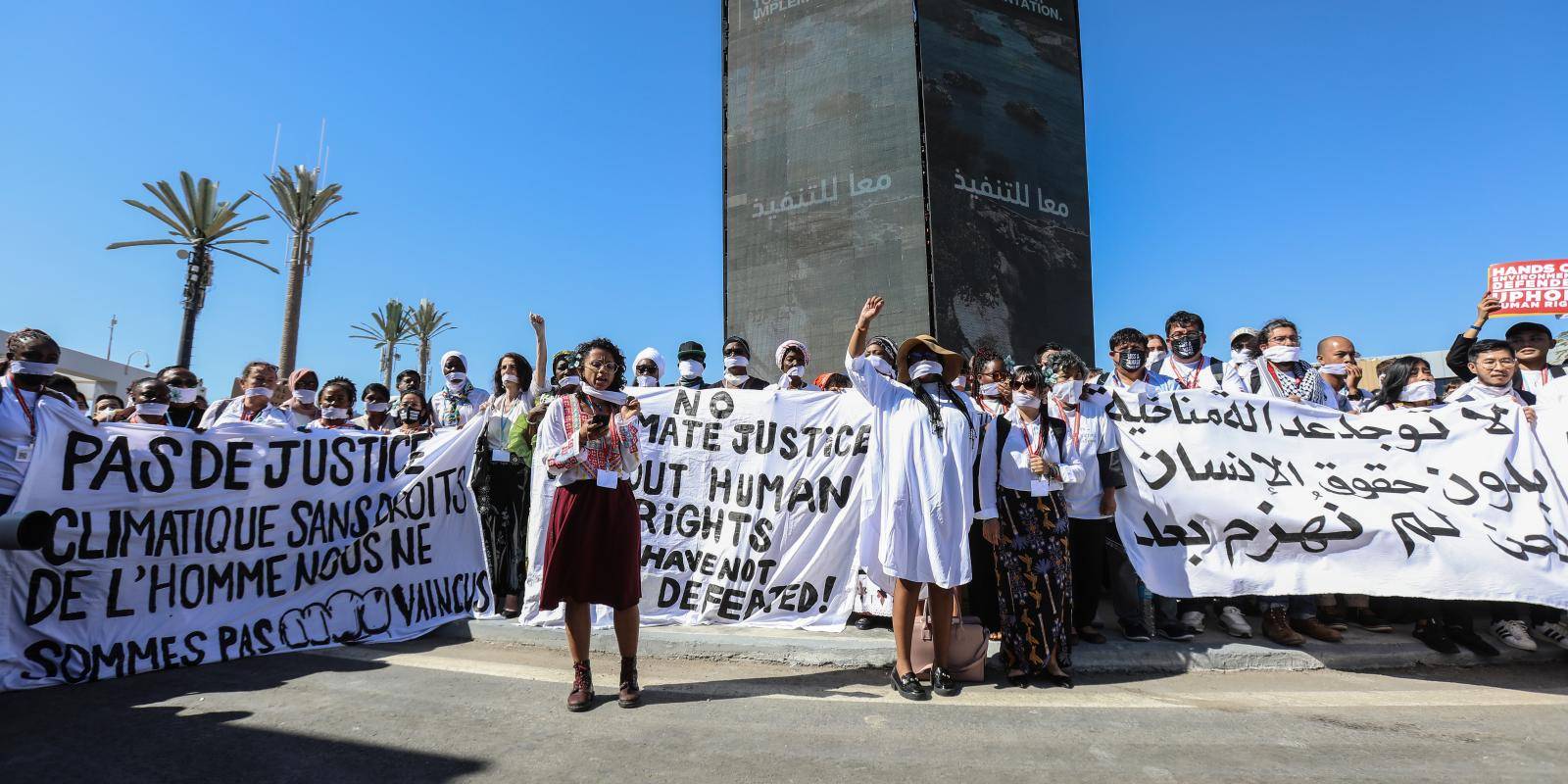 Women wearing white holding banners with the slogan No Climate Justice Without Human Rights against a blue sky in Sharm El-Sheikh, Egypt