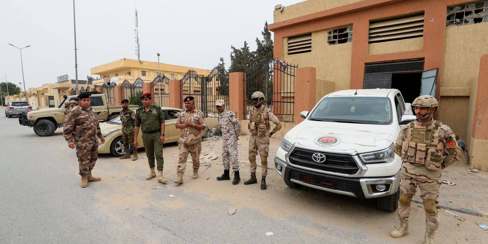 seven men each wearing a different military uniform stand beside a white vehicle parked on a street in Zawiya, Libya
