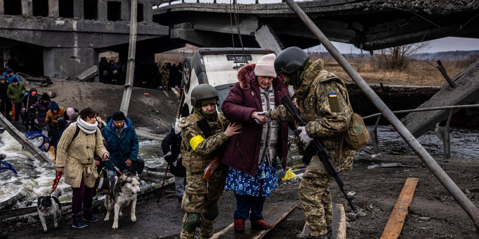 Ukrainian soldiers helping an elderly woman and other people to cross a destroyed bridge in the city of Irpin