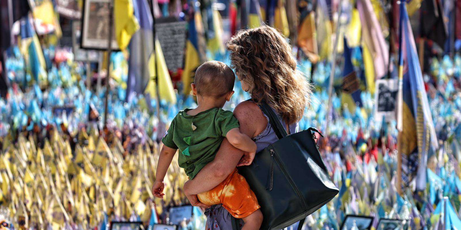 Woman and child stand in front of war memorial in Ukraine
