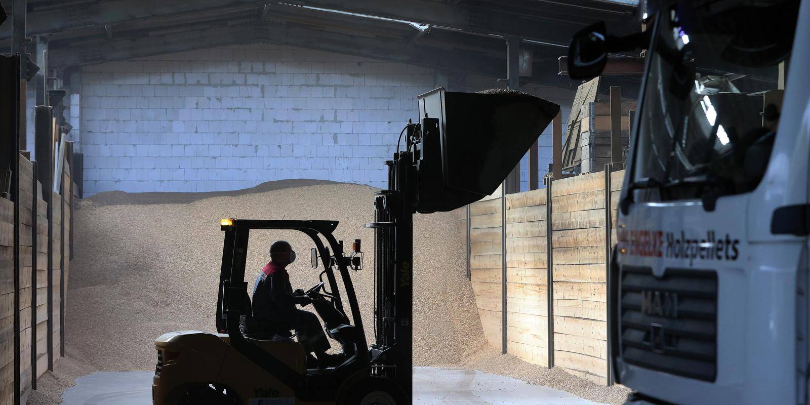 A man driving a forklift truck in a depot housing a pile of wood pellets 