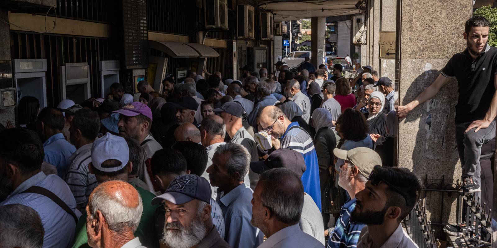 Crowds await outside a bank to withdraw money before Syria rejoins SWIFT