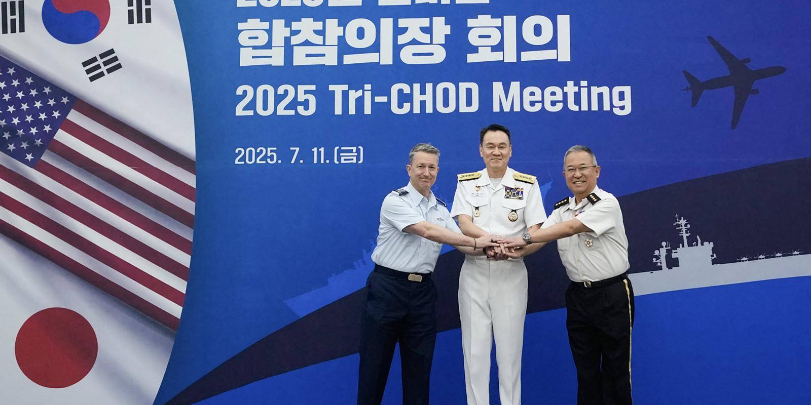 Three military leaders in uniform stand in front of a backdrop with the name and date of the meeting. The flags of South Korea, the US and Japan are visible to the left.