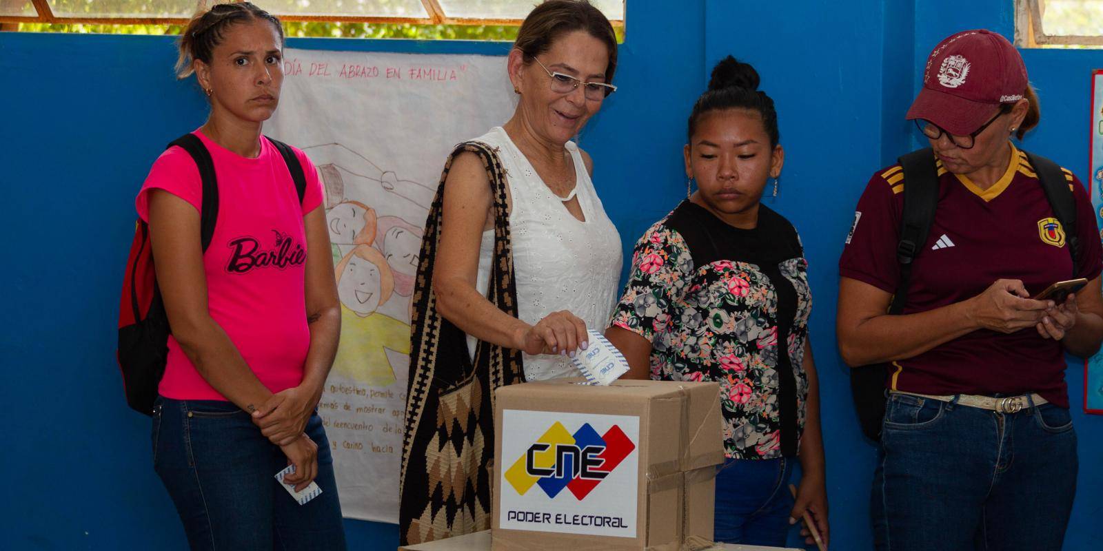 A group of voters standing by a box reading CNE. One woman is casting her ballot.