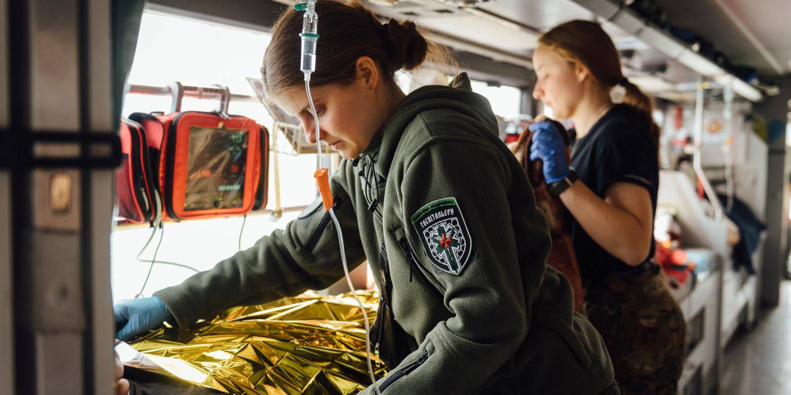 Two women medics in green uniforms attending to patients on a train in Ukraine