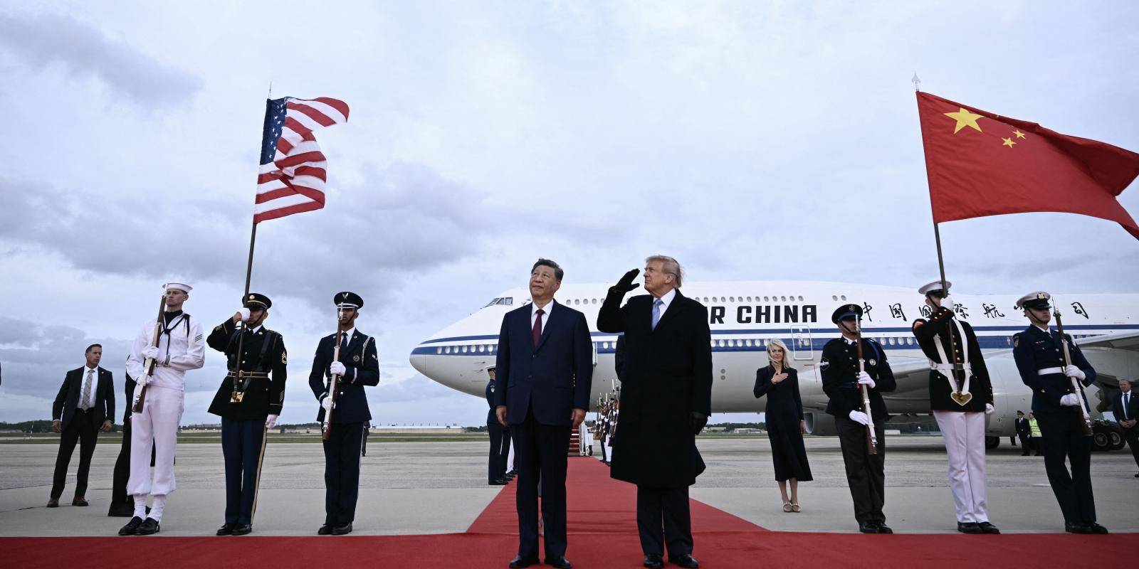 President Trump and President Xi stand on an airplane runway watching a jet fly over