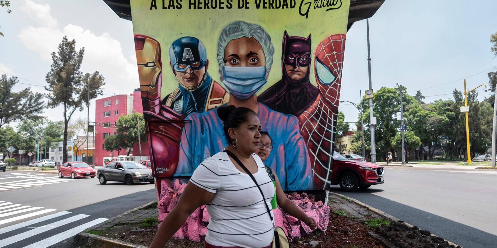 A woman walks past a mural showing a health worker and US superheroes, in Mexico City, on 21 July 2020. Photo credit: Copyright © Pedro Pardo/Getty Images