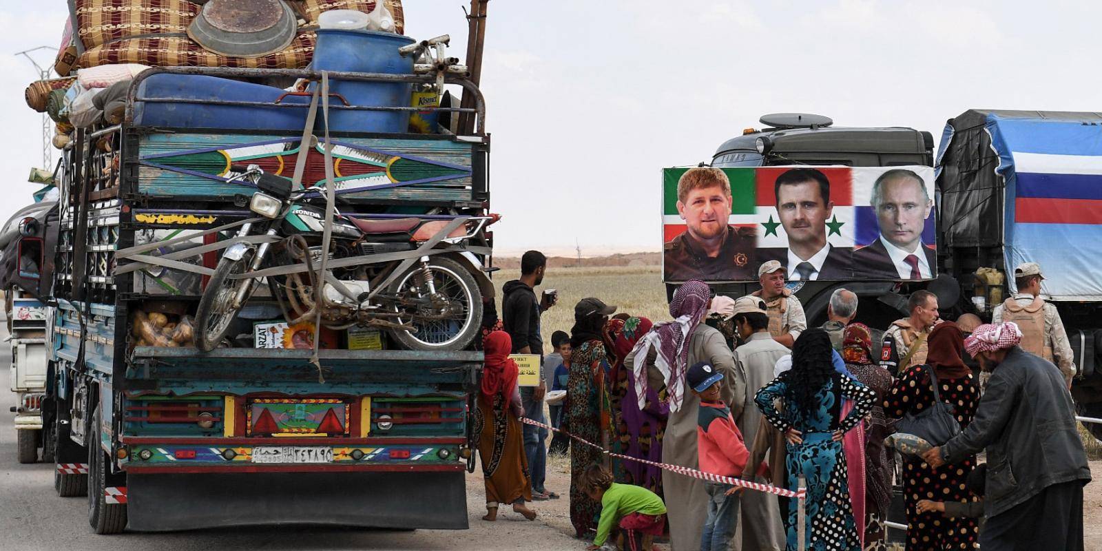 Members of the Russian military police hand out food aid to displaced Syrians returning into government-controlled territory at a checkpoint in Idlib province, 1 June 2018. A banner shows portraits of Chechen leader Ramzan Kadyrov, Syrian President Bashar al-Assad and Russian President Vladimir Putin. Photo: George Ourfalian/AFP/Getty Images