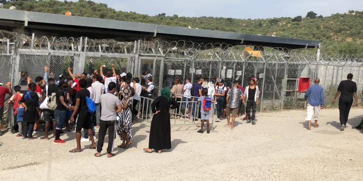 Photo of people crowding a barbed wire fence at the entrance of Moria refugee camp on Lesvos. Photo by Anna Iasmi Vallianatou