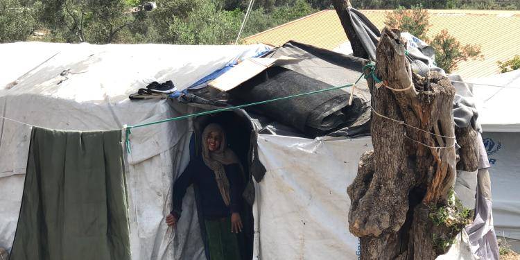Photo of a group of a dwelling made of cloth with a young woman standing at the entrance in Moria refugee camp on Lesvos. Photo by Anna Iasmi Vallianatou
