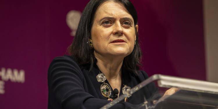 Bronwen Maddox standing at a lectern during her director's lecture.