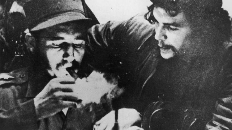 Fidel Castro (left) lights his cigar while Argentine revolutionary Che Guevara looks on in the early days of their guerrilla campaign in the Sierra Maestra Mountains of Cuba, circa 1956. Photo by Hulton Archive/Getty Images.