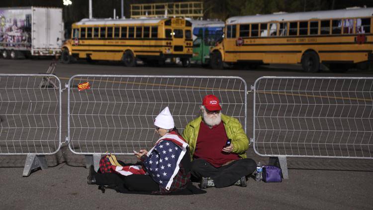 Two Trump supporters sitting down and using their phones