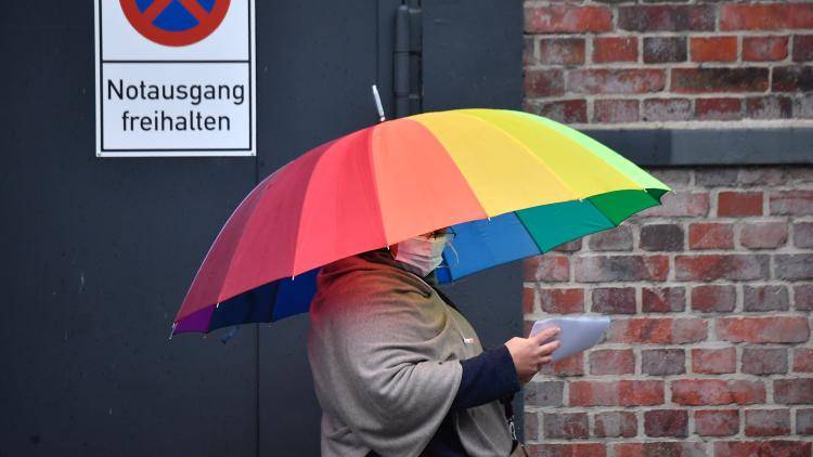 A person stands under a rainbow umbrella