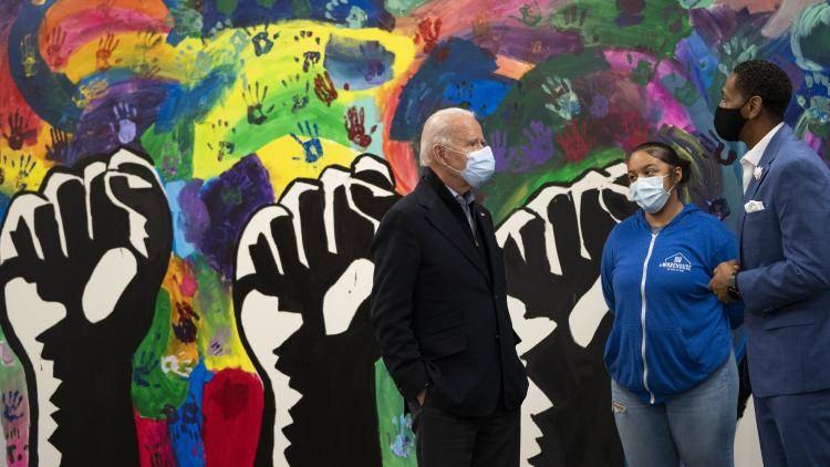 Joe Biden standing with two people in front of a mural