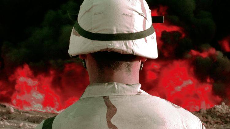 US soldier with his back to the camera and looking at a fire caused by an erupted pipeline