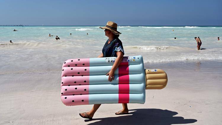 A person walks on the seashore with an inflatable mattress 