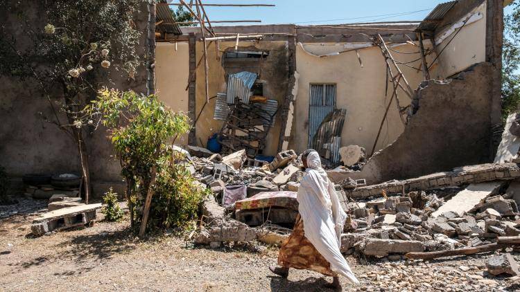 A woman walks in front of a destroyed house