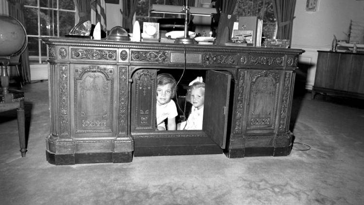 The Resolute Desk in the Oval Office with two children hiding in the central compartment