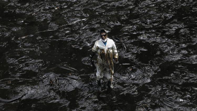 A member of a cleaning team gets to work on the Ventanilla shoreline just north of Lima covered in crude oil after the pipeline rupture
