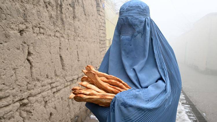 A woman wearing a burqa walks along a road towards her home after receiving free bread distributed as part of the Save Afghans From Hunger campaign in Kabul on 18 January 2022. Photo by WAKIL KOHSAR/AFP via Getty Images.