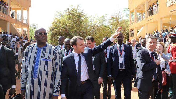 French President Emmanuel Macron salutes residents, walking with Burkina Faso's President Roch Marc Christian Kaboré, as he leaves Ouagadougou University after giving a speech, on November 28, 2017, in Ouagadougou, as part of his first African tour since taking office