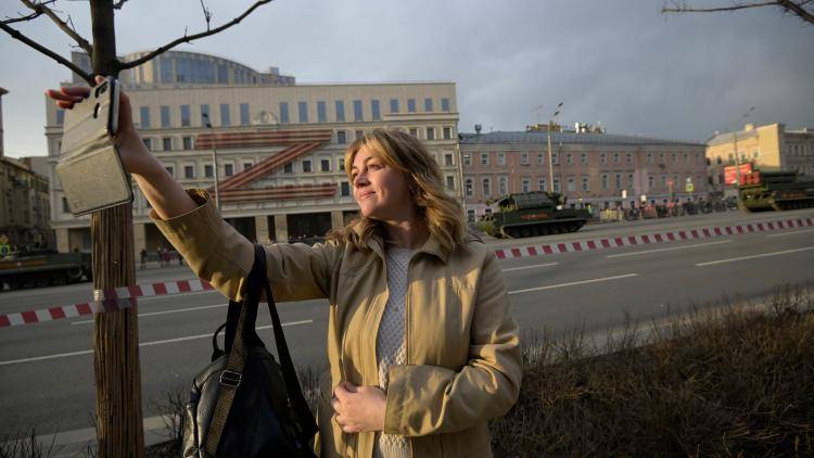 A woman uses her smartphone as she watches military vehicles heading to the Red Square for a rehearsal of the Victory Day military parade in central Moscow on 28 April 2022.