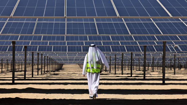An Emirati man walks beneath photovoltaic panels at al-Dhafra Solar Photovoltaic (PV) Independent Power Producer (IPP) project south of the capital Abu Dhabi, on 13 November 2023. Photo by KARIM SAHIB/AFP via Getty Images.