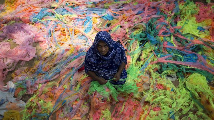 A woman sits on a huge pile of colourful textile waste in Dhaka, Bangladesh, 23 May 2017