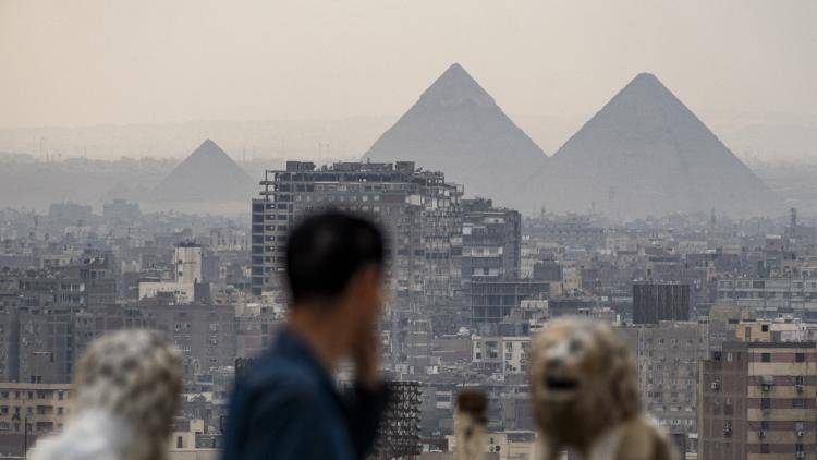 The Great Pyramid of Khufu (Cheops) and the Pyramids of Khafre (Chephren) and Menkaure (Menkheres) in Giza are visible in the background as a tourist walks at the promontory of the Cairo Citadel overlooking the skyline of Cairo and its twin city of Giza on 19 February 2024. 
