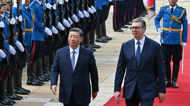 Serbian President Aleksandar Vucic walks with Chinese President Xi Jinping along a red carpet, past Serbian soldiers standing to attention 