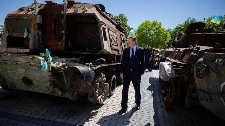 David Cameron stands between two burned-out Russian military vehicles