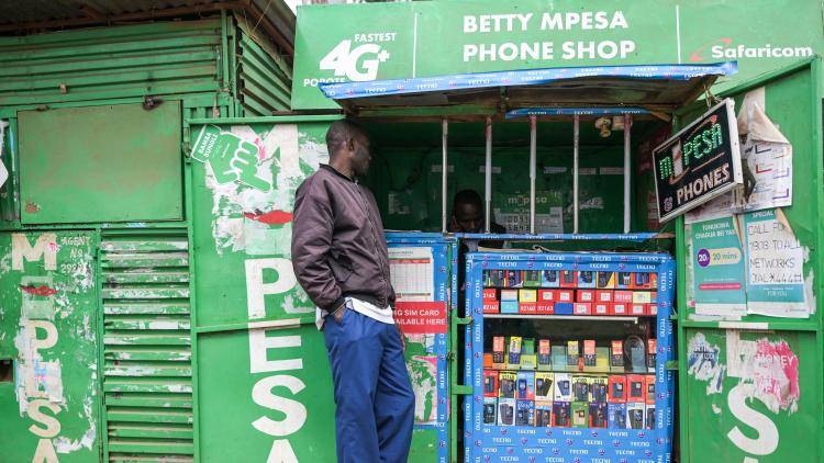 A man stands next to a bright green phone shop in Nairobi