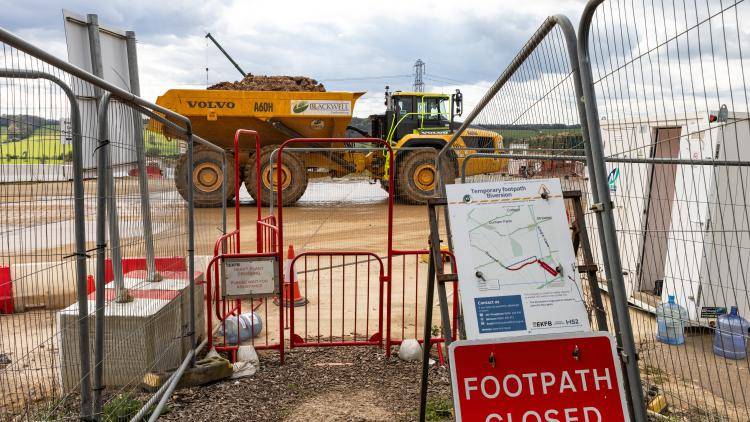 A yellow dumper truck passes behind a red footpath closure sign 