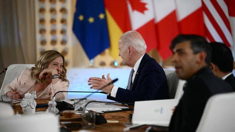 Italy's Prime Minister Giorgia Meloni leans towards US President Joe Biden across a table, with flags in the background, at the G7 summit in Italy.