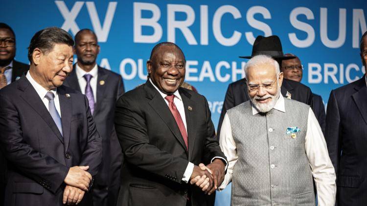 three men in suits stand on stage shaking hands 